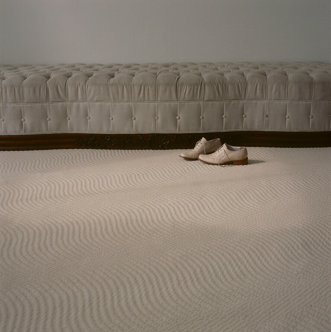 Pair of men's shoes next to a upholstered sofa in a neutral coloured carpeted living room