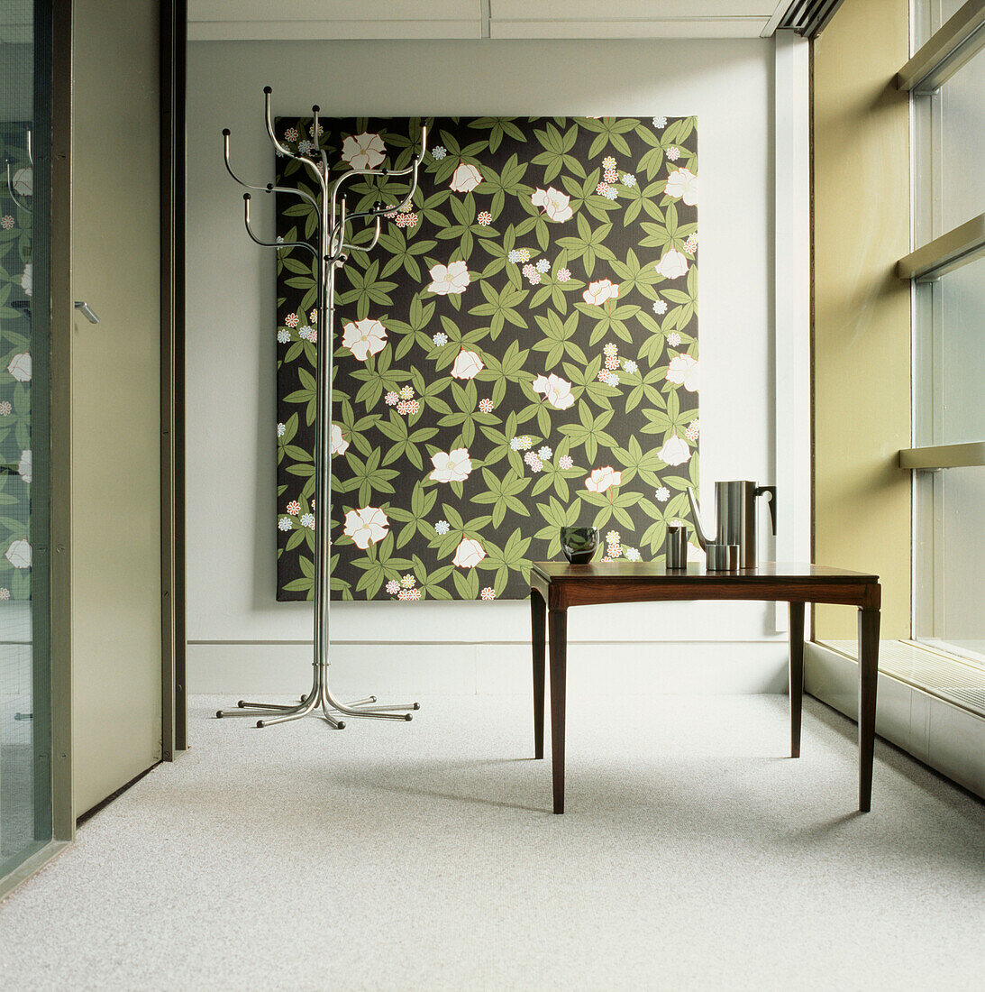 Zeitgenössischer Flur mit Garderobenständer aus Metall, Holztisch, grünem Blumendruck auf Leinwand, Glaswänden und neutralem Dekor