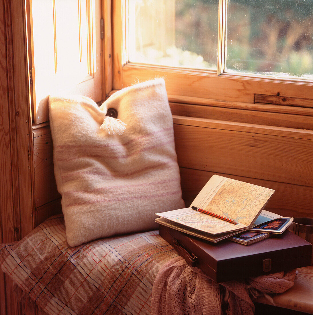 Holzgetäfelte Fensterbank im Stil der Zeit mit Kissen, Wolldecke und Lesestoff