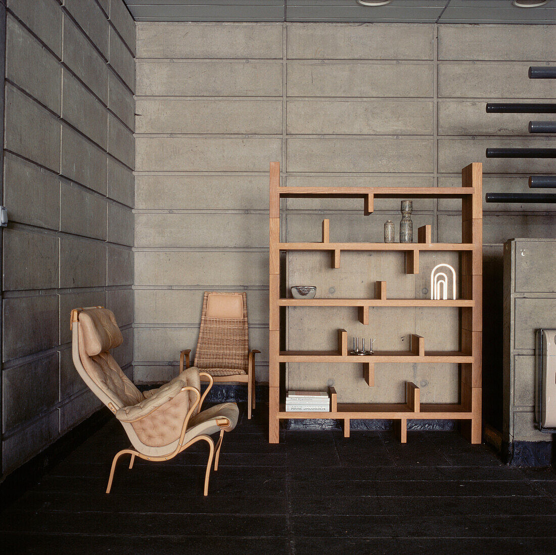 Living room with concrete wall panels retro chairs and free standing shelving unit