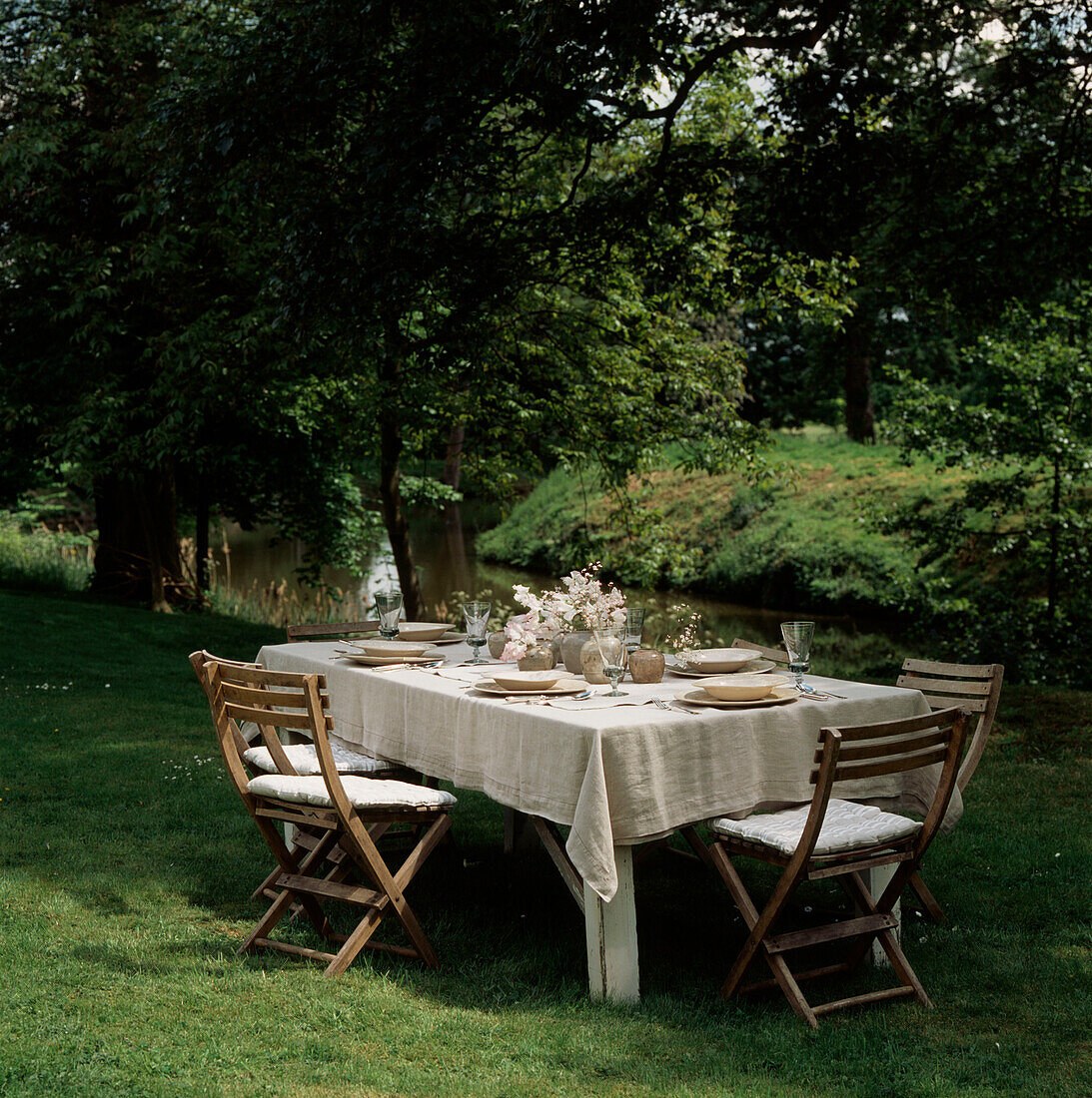 Gedeckter Tisch für eine Gartenparty an einem idyllischen Ort an einem von Bäumen gesäumten Fluss in der Sommerzeit