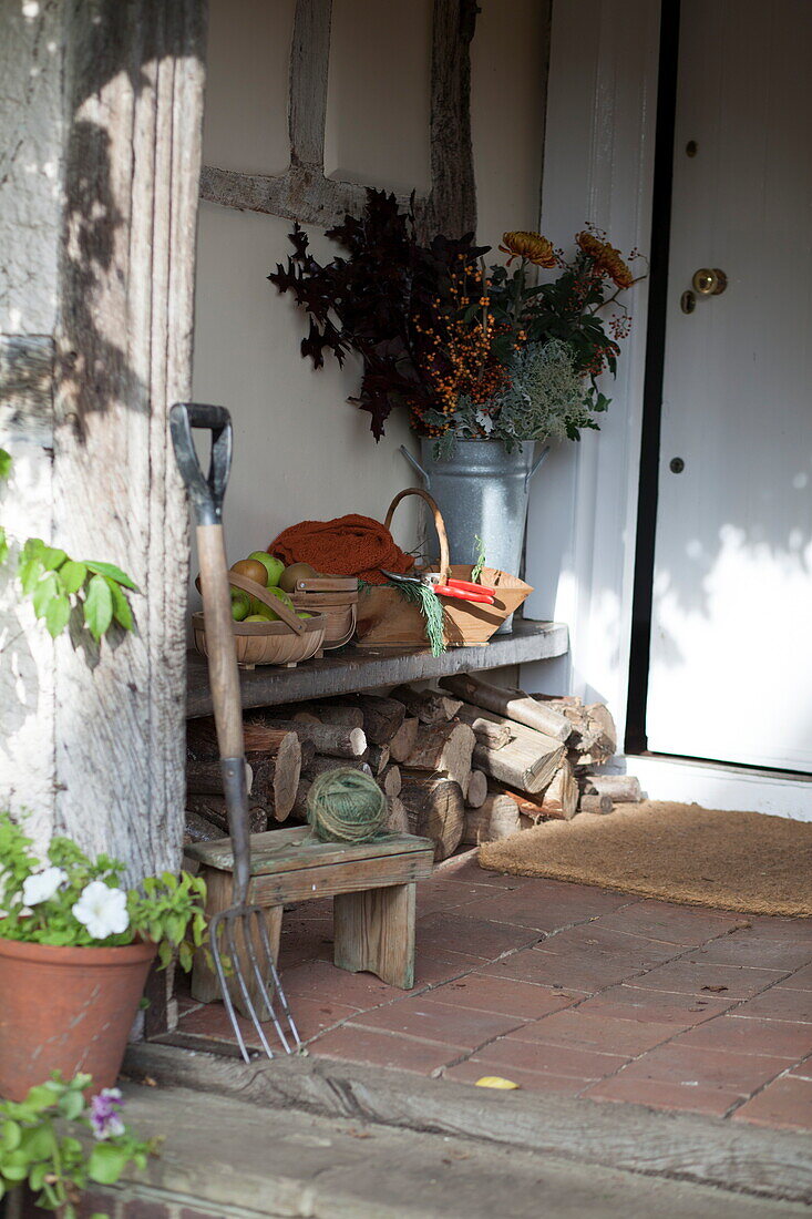 Firewood and doormat with garden fork in porchway of farmhouse, United Kingdom