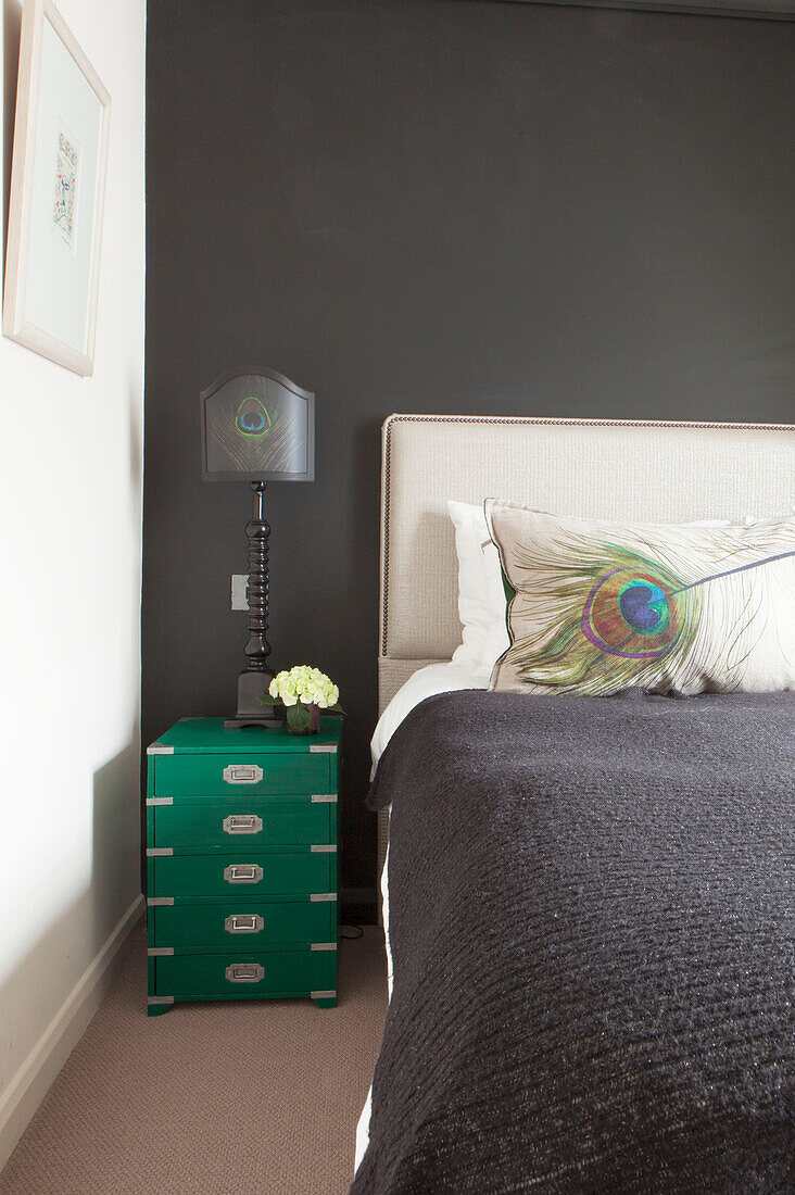 Pfauenfederkissen mit grünem Nachttisch im dunkelgrauen Schlafzimmer einer modernen Londoner Wohnung England UK