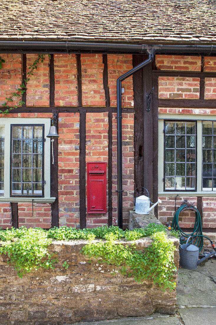 Briefkasten in einem Bauernhaus mit Fachwerk und Gießkannen Surrey England UK