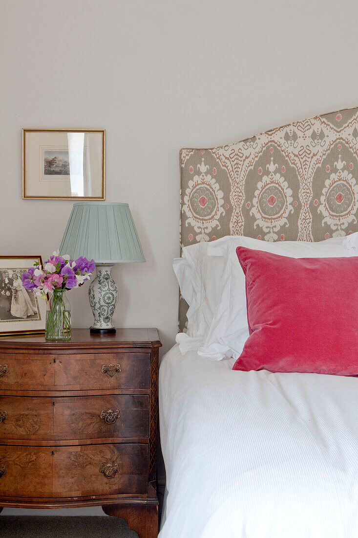 Rosa Kissen auf dem Bett mit antiker Kommode in einem Landhaus in Wiltshire, England UK