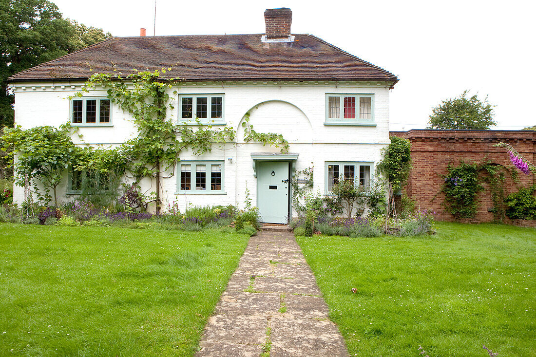 Fußweg im Rasen zur Eingangstür eines weiß getünchten Cottages in Surrey England UK