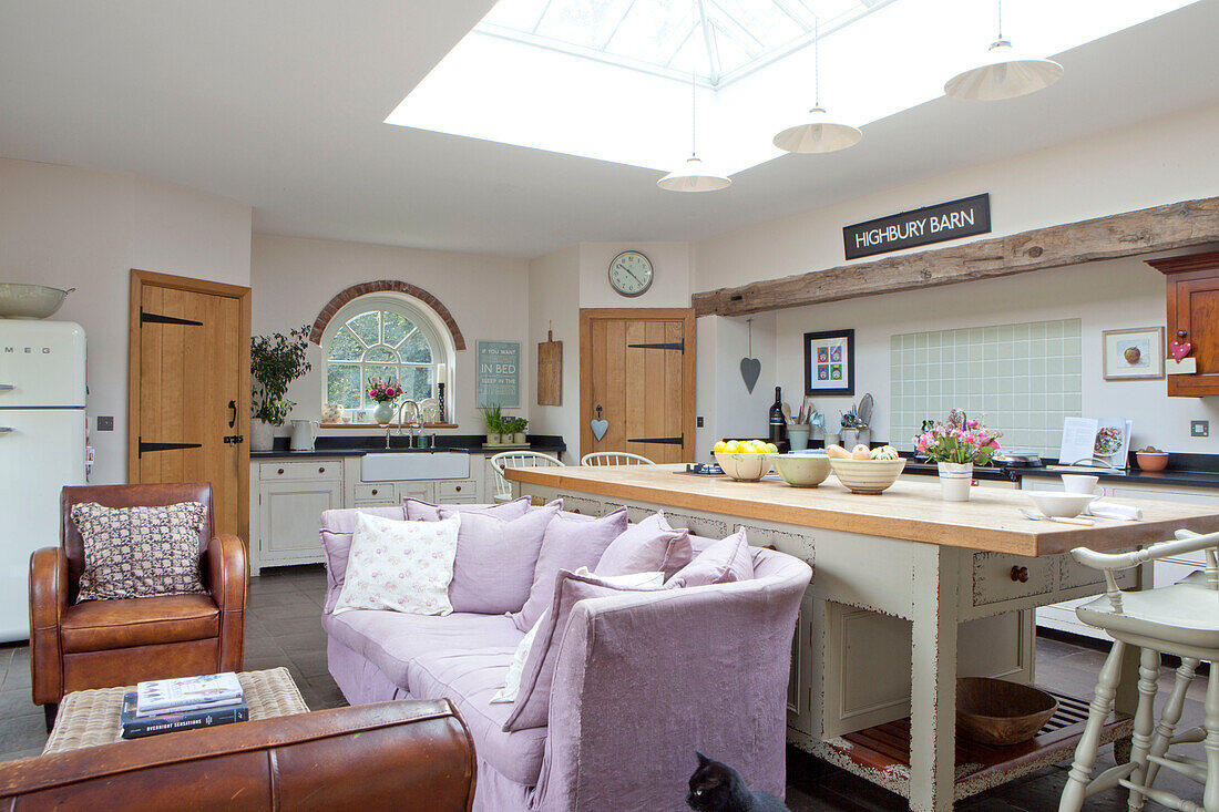 Lilac sofa in open plan kitchen with skylight in Surrey cottage England UK