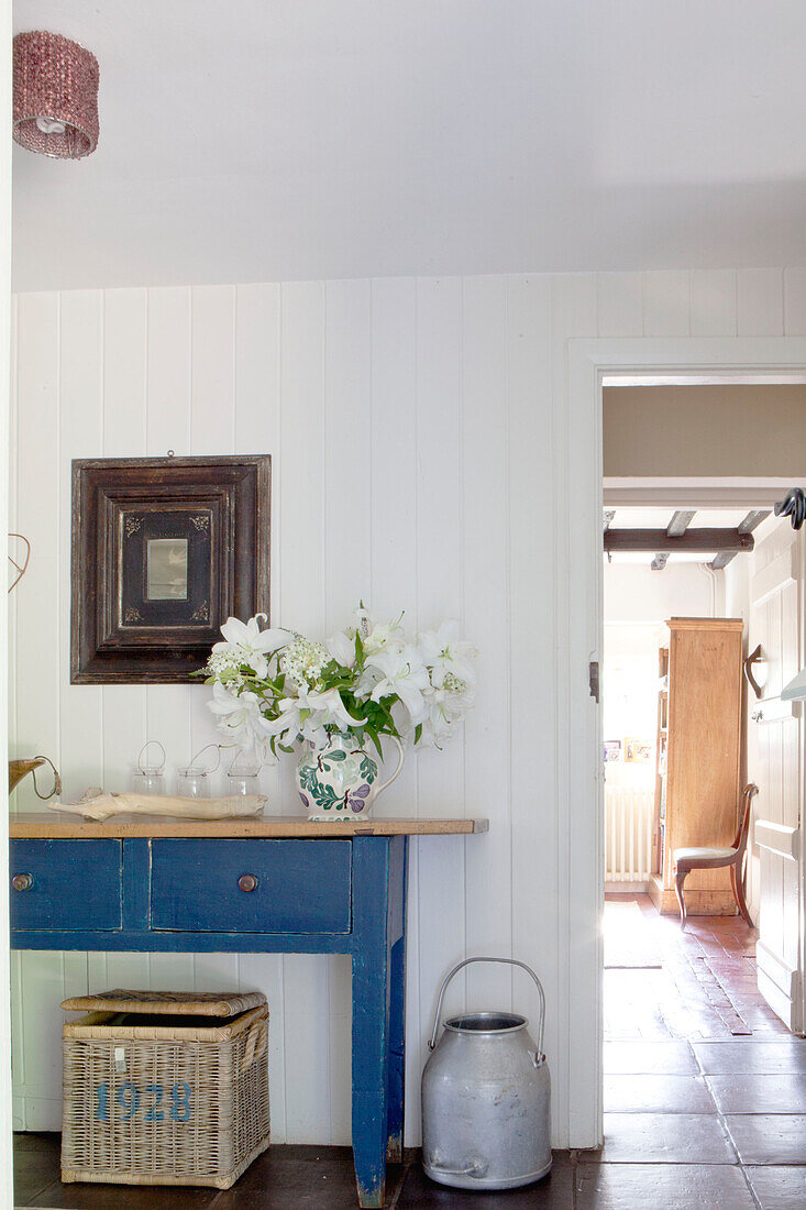 Milk pail and basket with blue painted table in hallway of Surrey cottage England UK