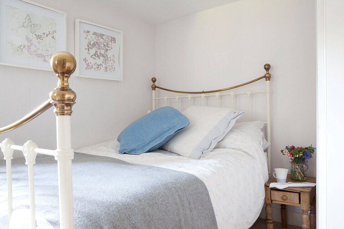 Einzelbett aus Messing mit blauem Kissen und Nachttisch aus Holz in einem Cottage in Surrey, England UK