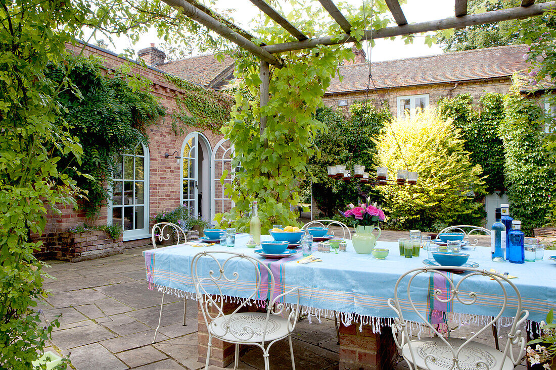 Blue tablecloth on patio table with wrought iron chairs in courtyard garden of Surrey cottage England UK