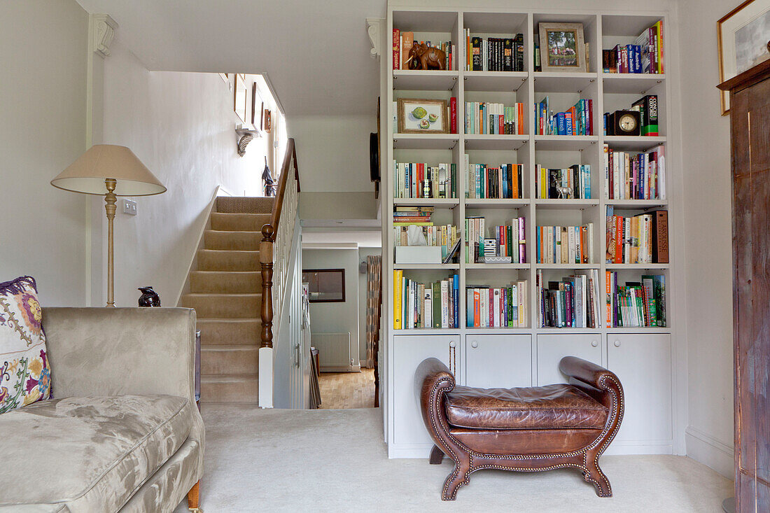 Bookcase with brown leather stool on staircase landing of contemporary Chelsea home London UK