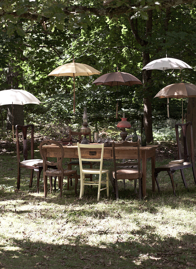 Sonnenschirme beschatten Tisch und Stühle in einem bewaldeten Garten, UK