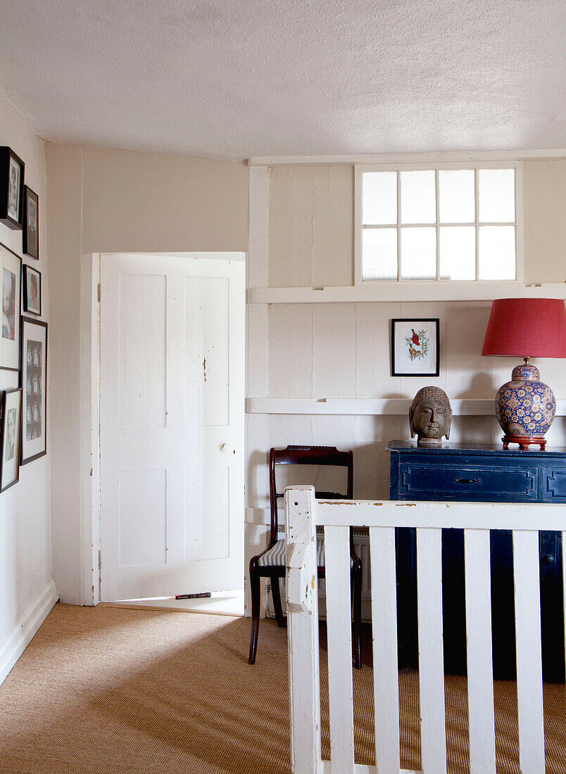 Antique chair and blue painted sideboard with wall mounted photographs in entrance hallway of UK home