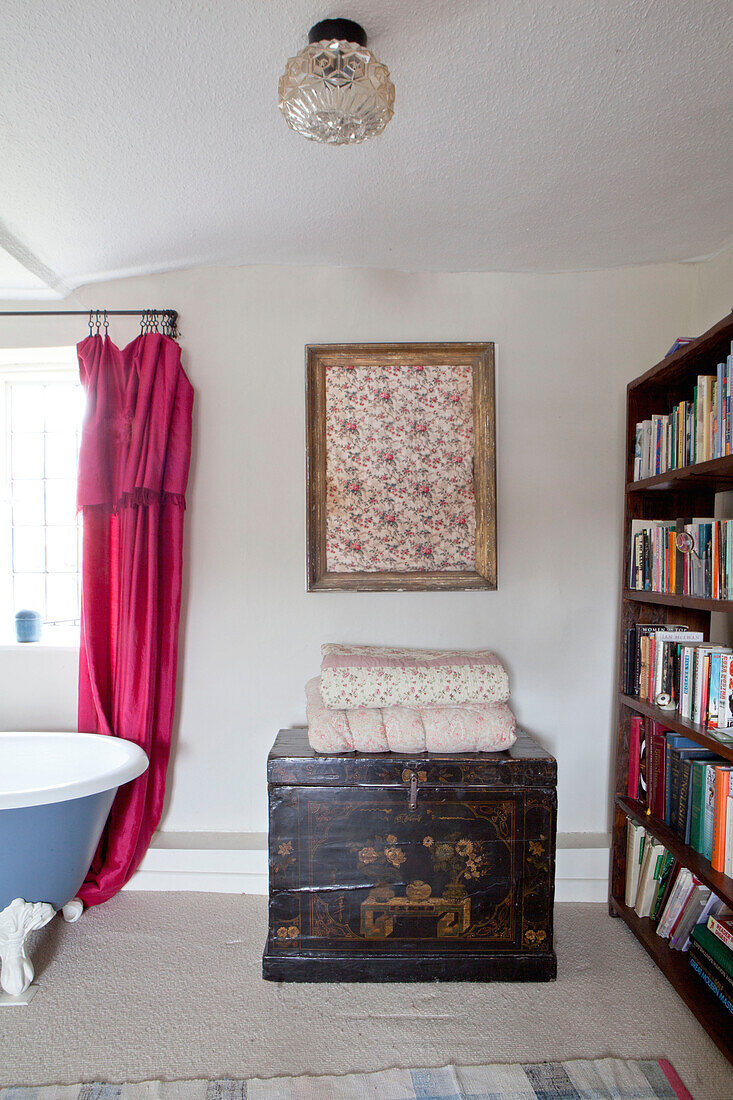 Gerahmtes Stoffmuster mit gefalteten Steppdecken auf orientalischer Truhe und Bücherregal im Badezimmer eines britischen Hauses