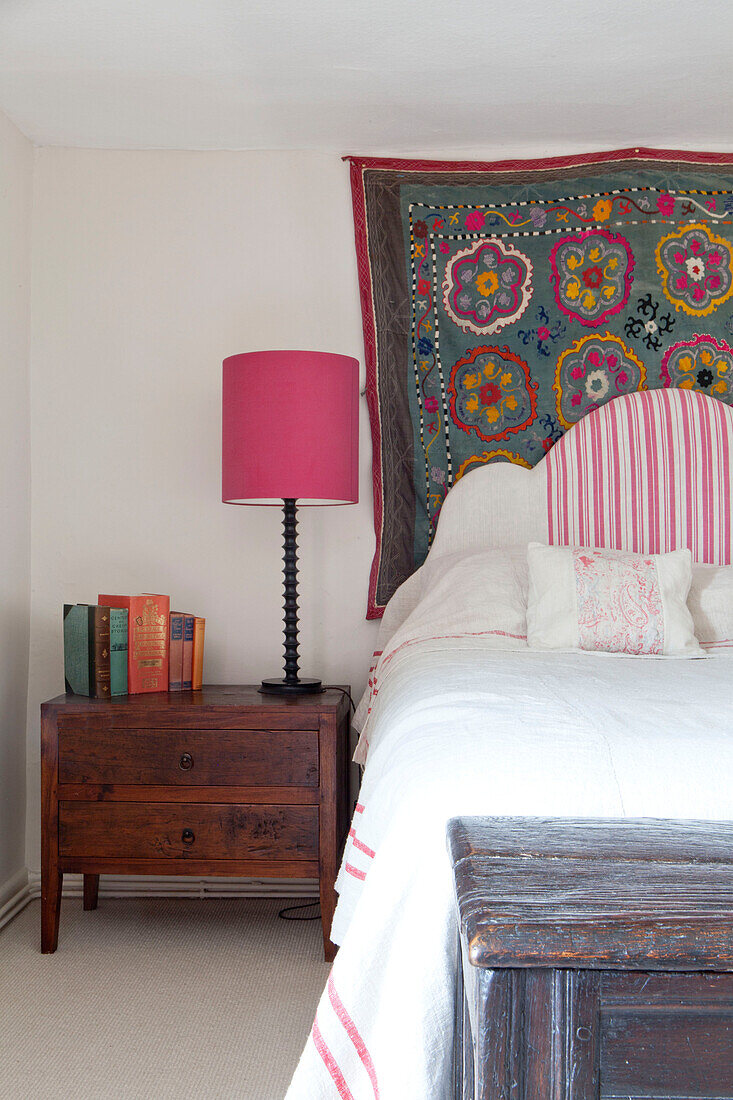 Floral bestickter Wandbehang über dem Bett mit hölzernem Nachttisch in einem Haus in Großbritannien