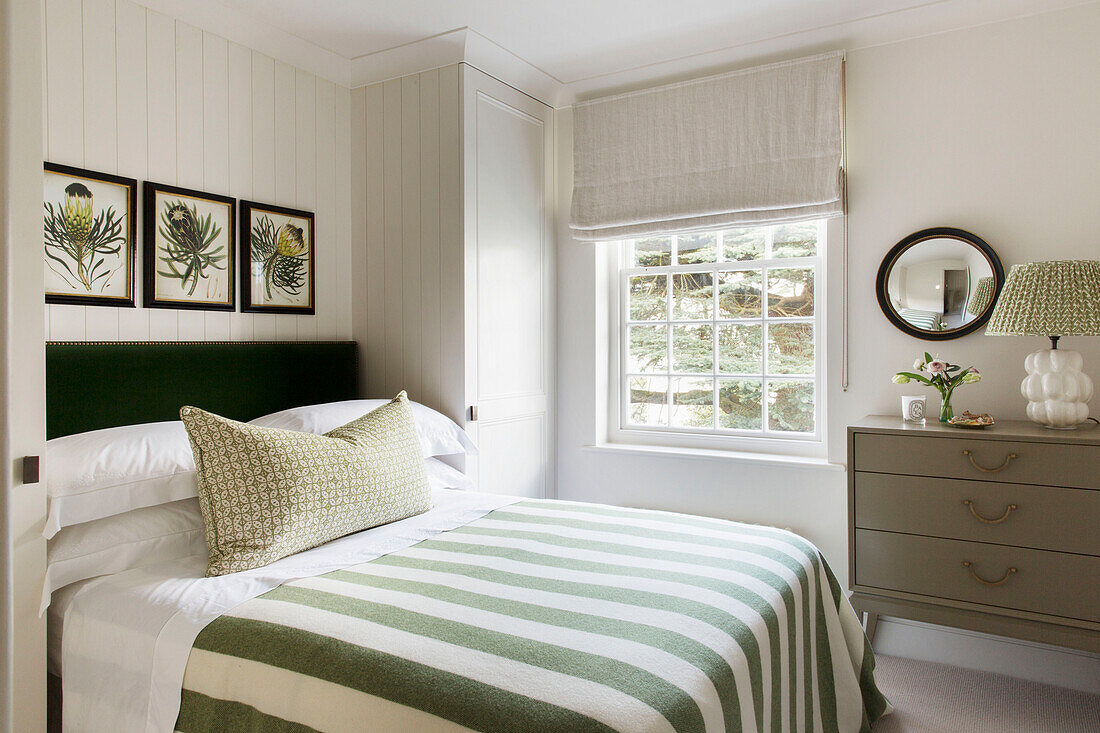 Green and white striped bed cover with Roman blinds at window in London home UK