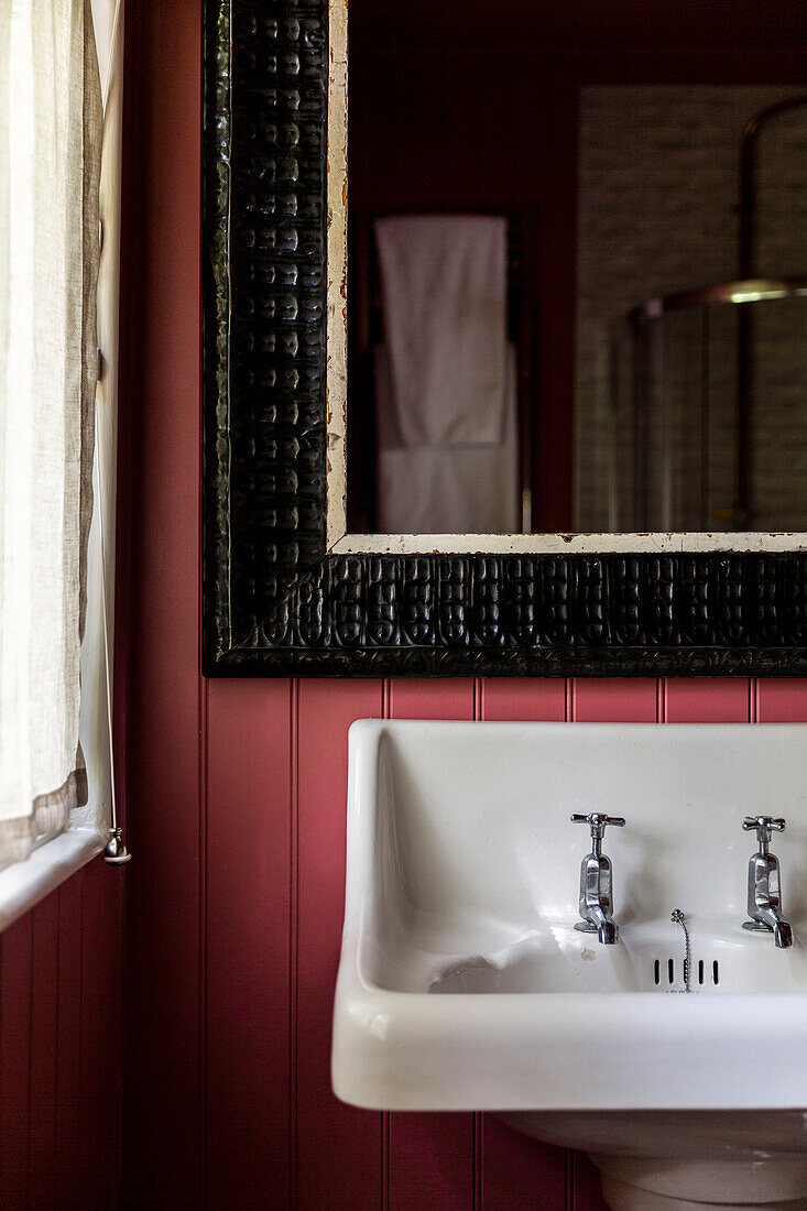 Pinkfarbene Nut- und Federbemalung und schwarzer Spiegelrahmen über dem Waschbecken in einem Haus in Cirencester, Gloucestershire, Großbritannien