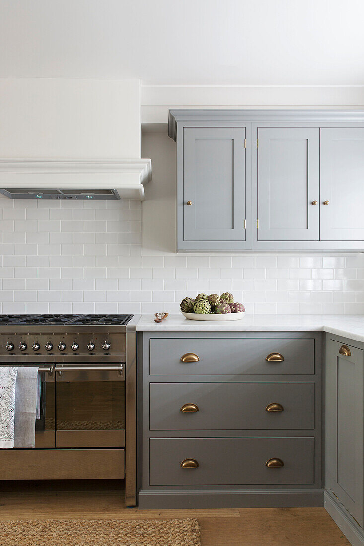 Gold fittings on light grey units with stainless steel oven in minimalist London kitchen UK