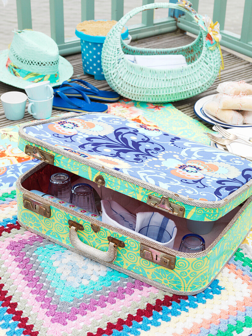 Vintage-Koffer auf Picknickdecke mit Flip Flops und Tassen