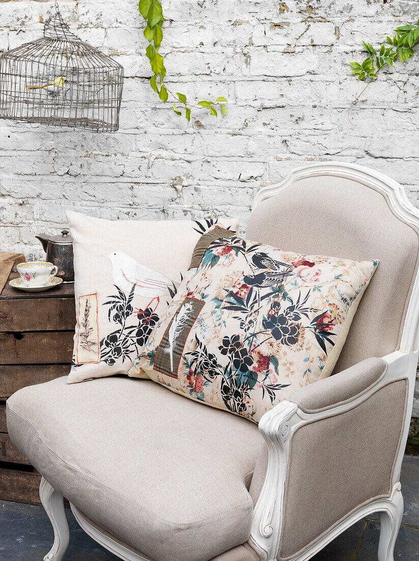 Blumenkissen und Vogelkäfig mit cremefarbenem Sessel in weiß getünchtem Raum Battersea London UK