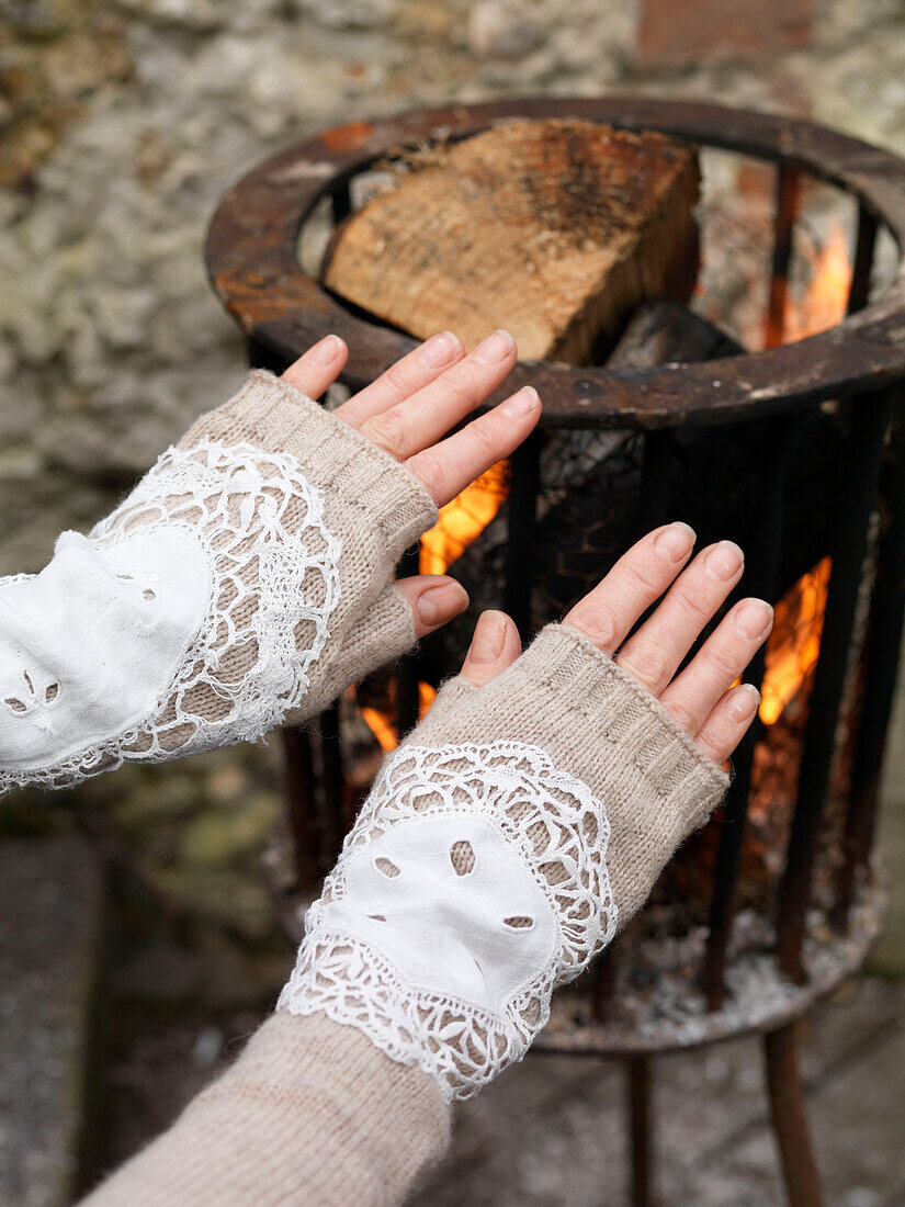 Woman warming hands at brazier with lace sleeve detail Brighton, East Sussex UK