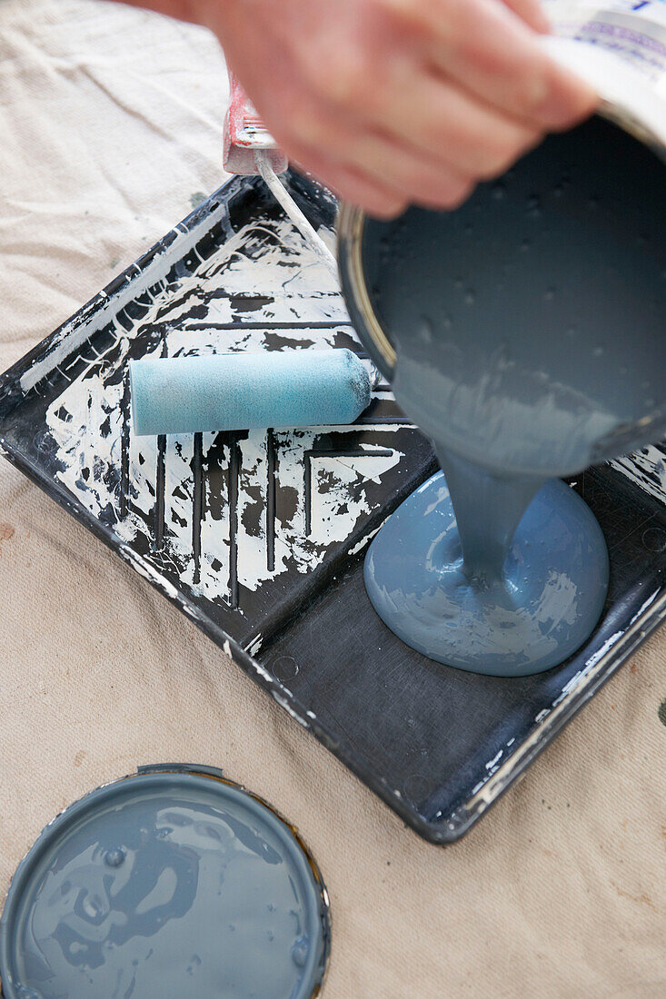 Frau gießt Farbe aus einer Dose auf ein Tablett in einem britischen Haus