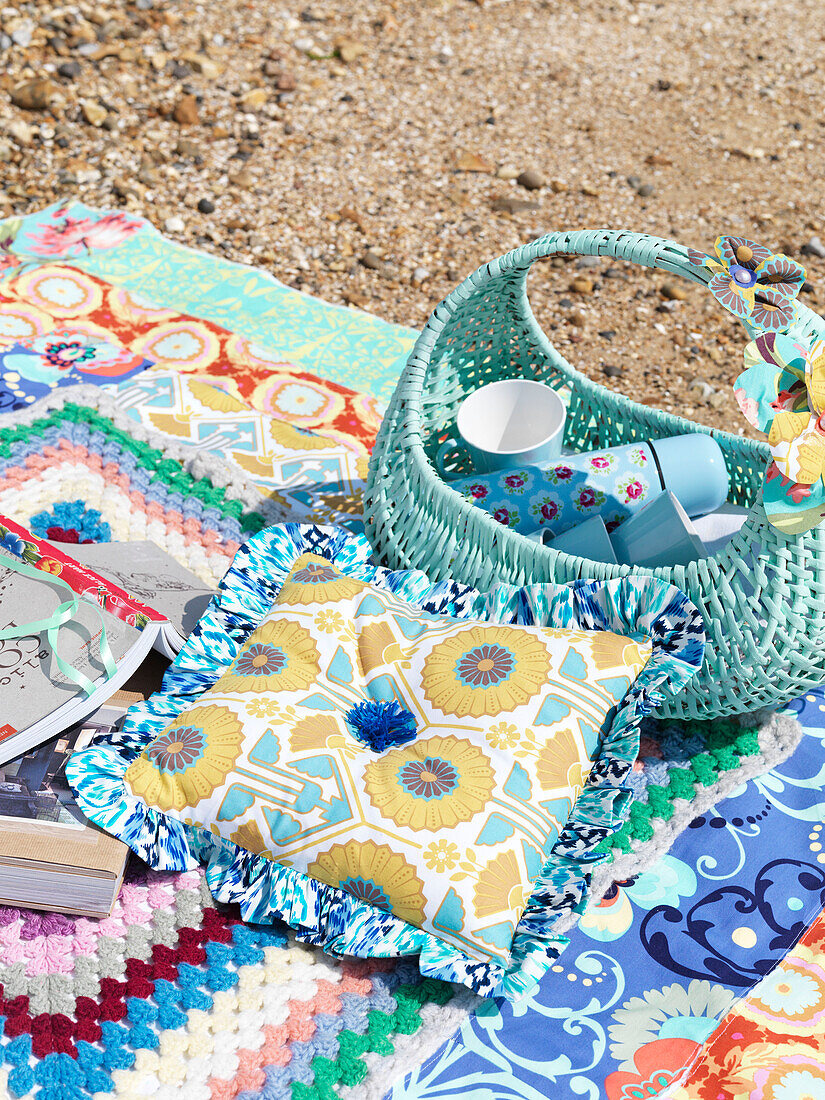 Gelbes Kissen mit türkisfarbenem Korb auf Picknickdecke am Strand