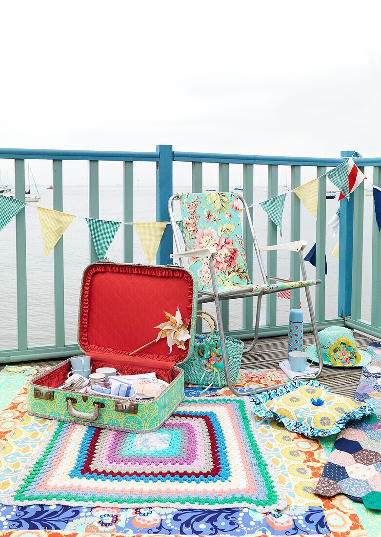 Folding chair and vintage suitcase on painted decking with bunting and blanket