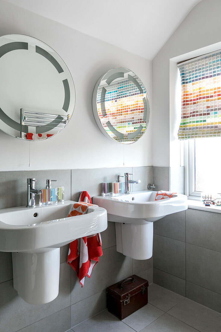 Runder Spiegel über einem Doppelwaschbecken mit farbigen Jalousien in einem Haus in Farnham, Surrey, Großbritannien