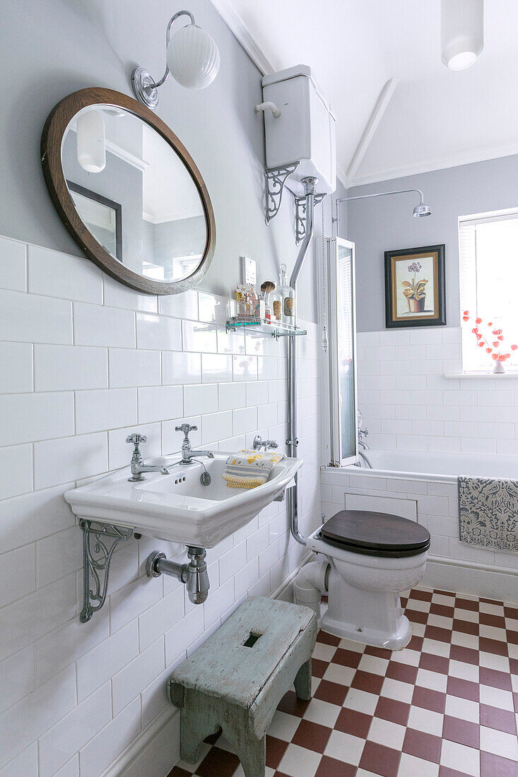 Holzspiegelrahmen über antikem Waschbecken mit Toilette und Spülkasten in gefliestem Badezimmer in Guildford, Surrey, Großbritannien