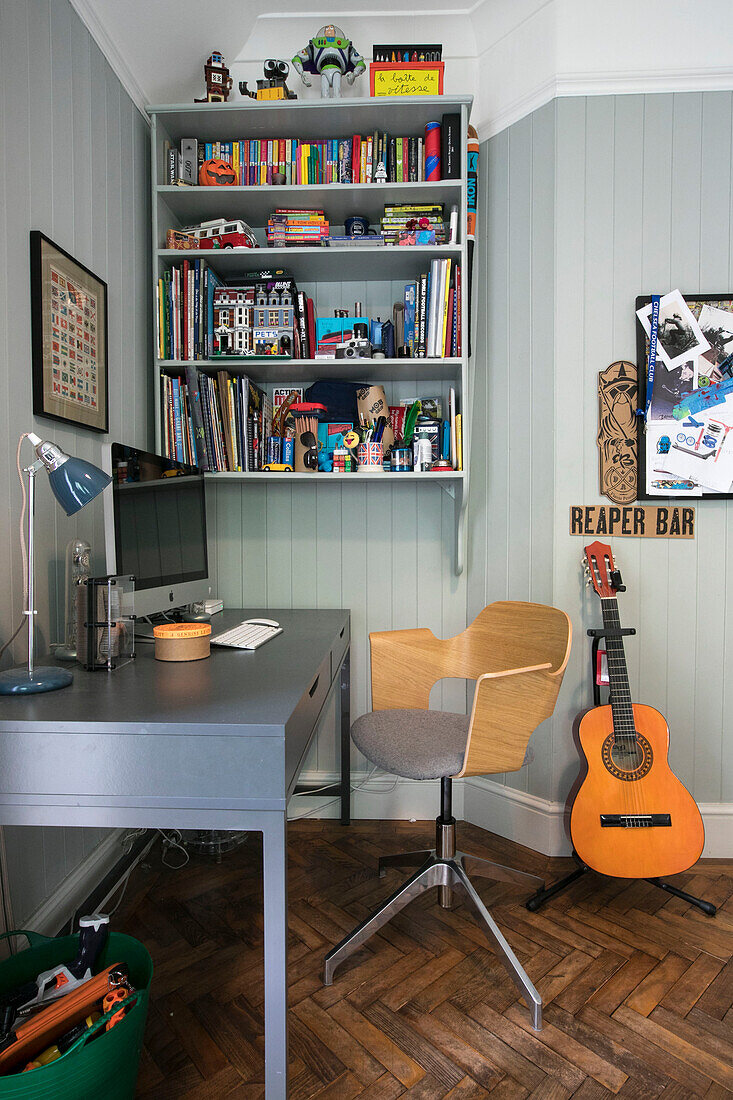 Schreibtisch und Stuhl mit Bücherregal und Gitarre im Jungenzimmer eines Hauses in Guildford, Surrey, Großbritannien