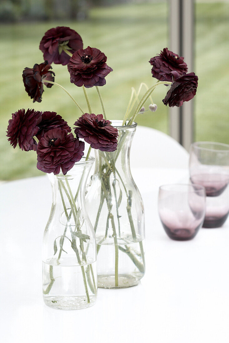 Zwei Vasen mit Blumen auf einem Tisch mit Gläsern