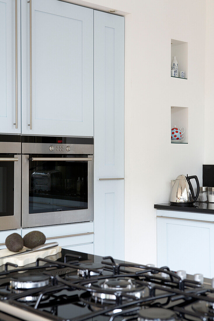 Pastellblaue Küchenschränke mit eingelassenen Regalen, Wasserkocher und Backofen
