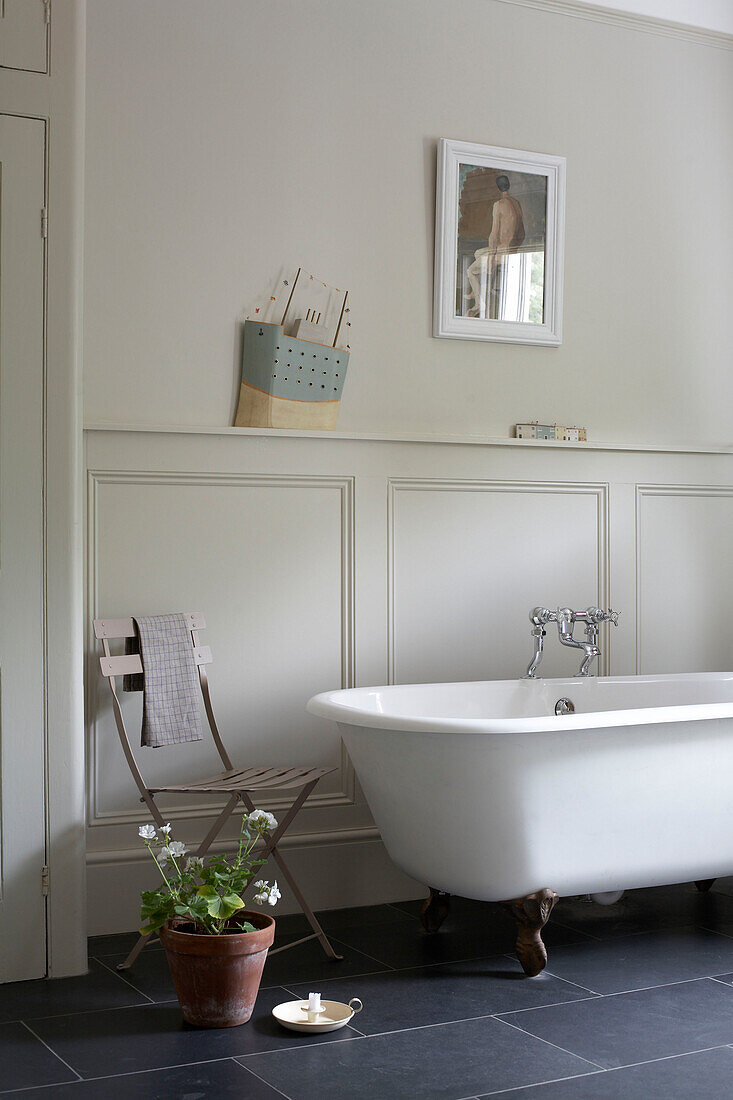 Panelled bathroom with freestanding roll-top and folding chair with houseplant