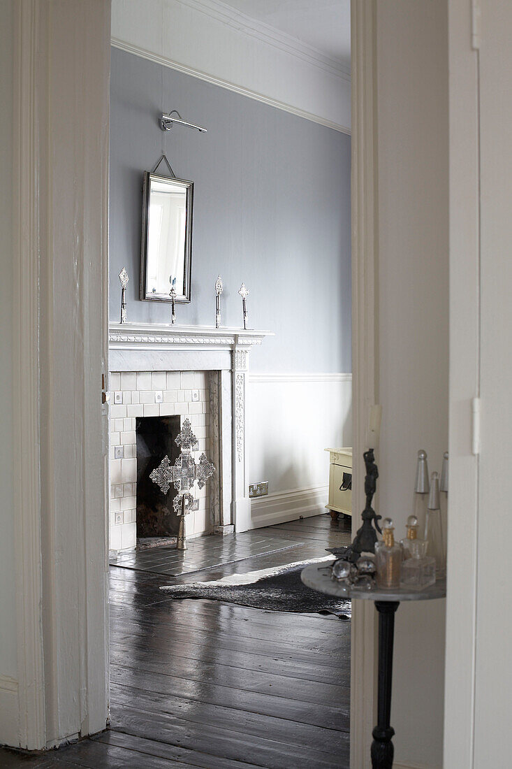 Blick durch die Tür zum Kamin in einem spärlich eingerichteten hellblauen Zimmer