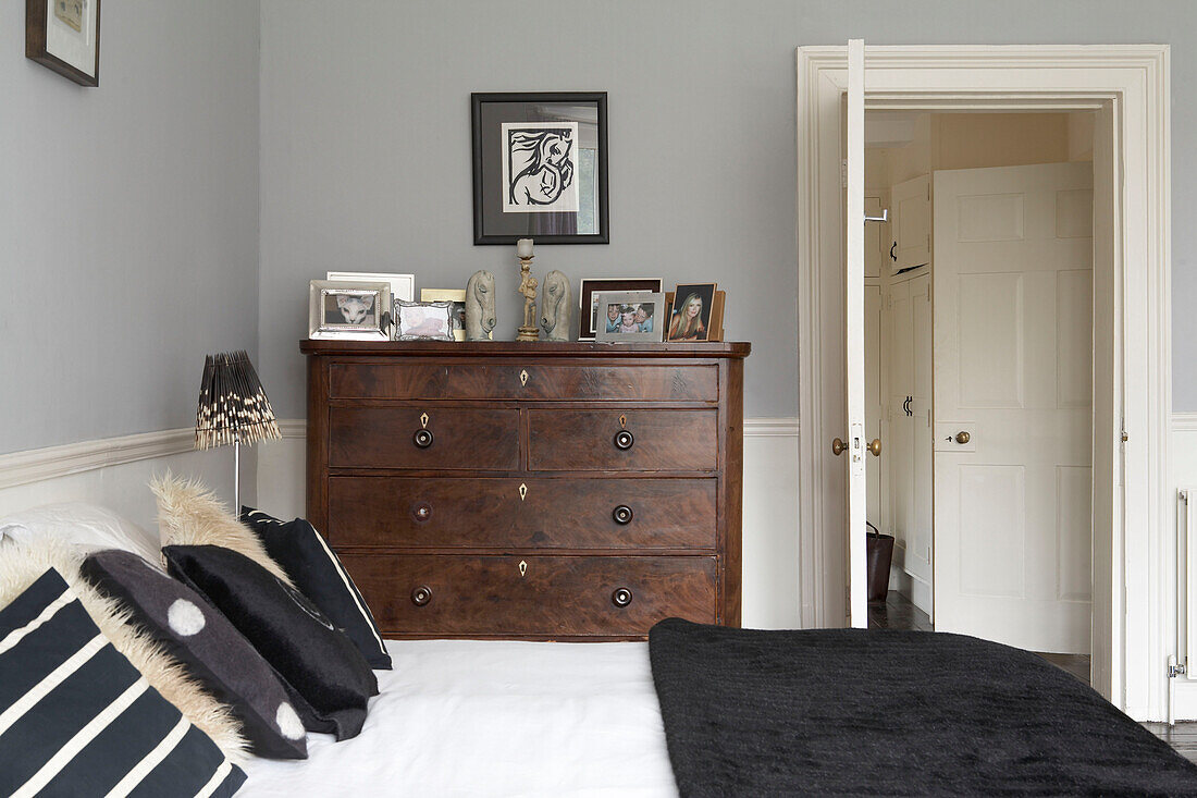 Schwarzer Bettbezug mit kontrastierenden Kissen und antiker Kommode im taubengrauen Schlafzimmer