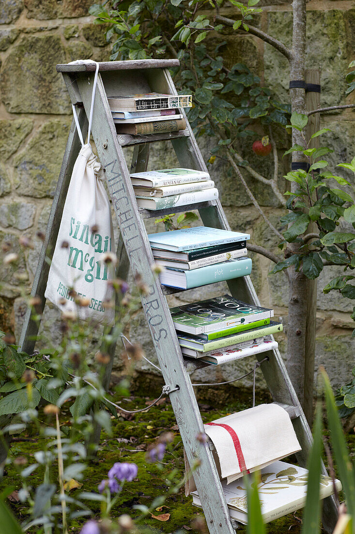 Bücherstapel auf Stufenleiter in ummauertem Garten mit Apfelbaum, St Lawrence, Isle of Wight, UK