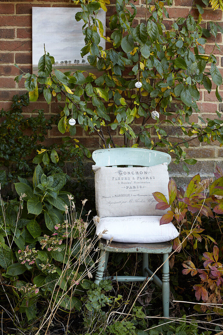 Stuhl und Kunstwerk im Blumenbeet an einer Backsteinmauer in St Lawrence, Isle of Wight, UK
