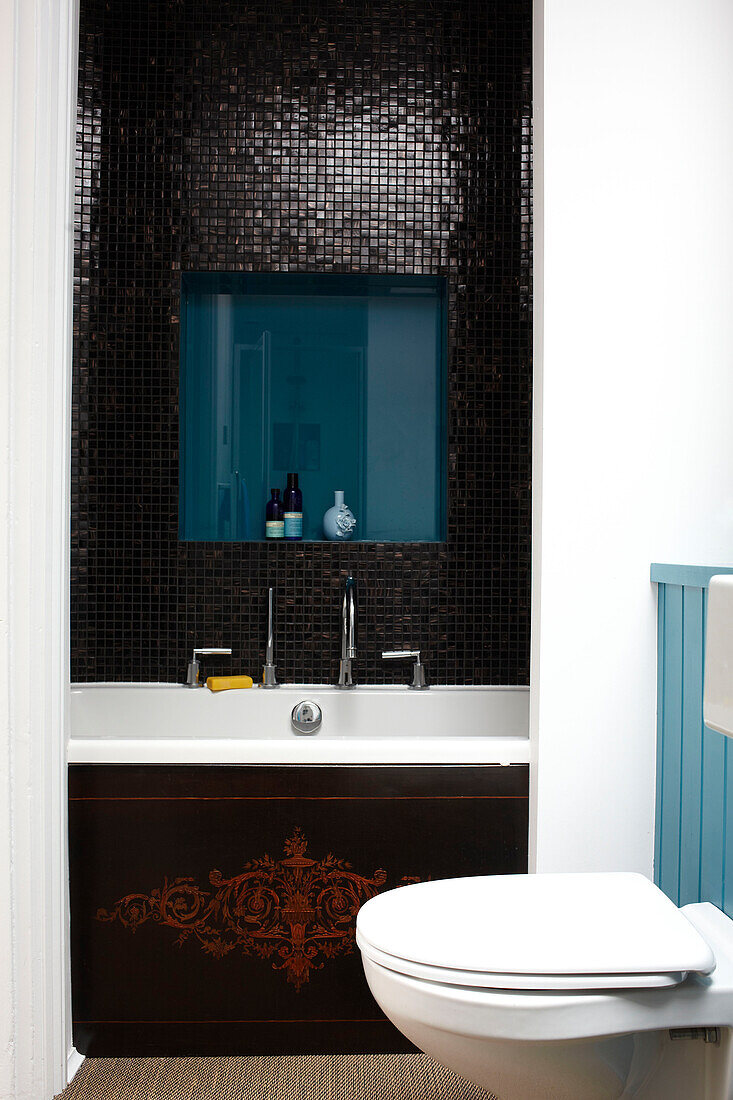 Mosaikgeflieste Badewanne mit Nische für Toilettenartikel in einem modernen Haus in Bristol, England, UK