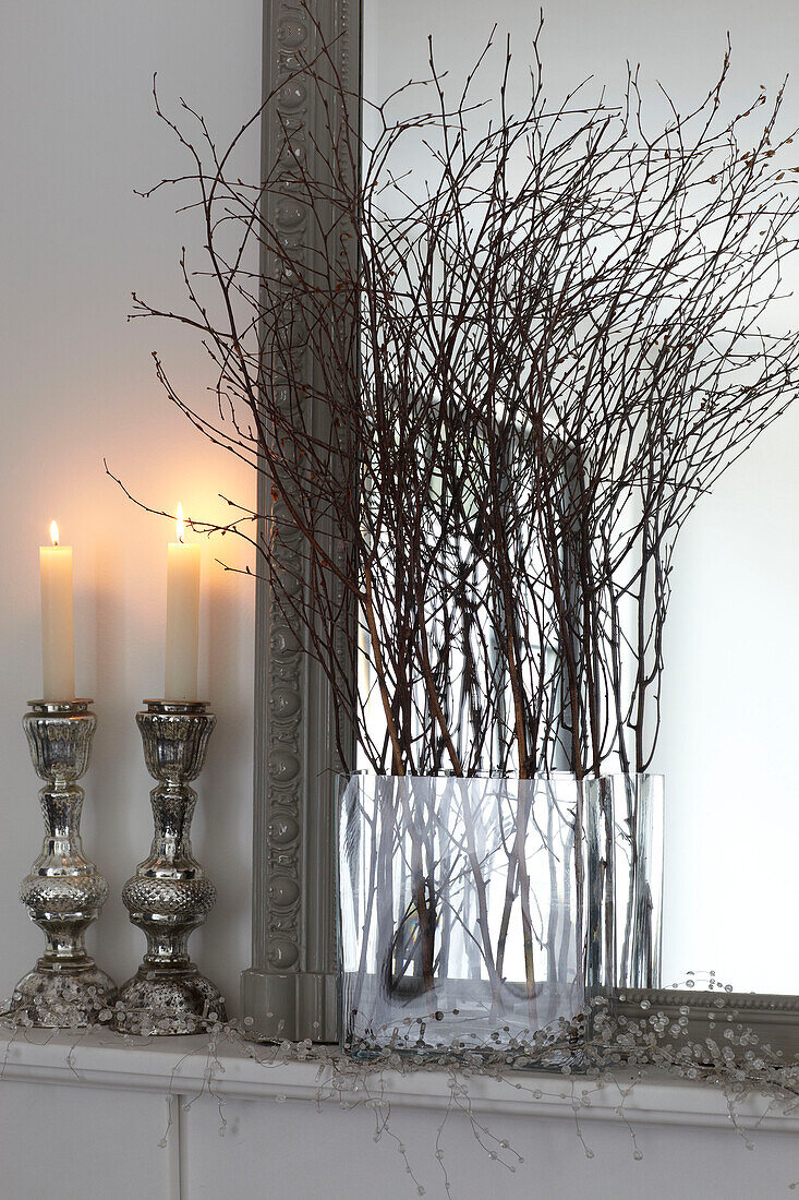 Anzündende Kerzen auf Marmorregal mit Zweigarrangement und Spiegel in einem Haus auf der Isle of Wight, UK