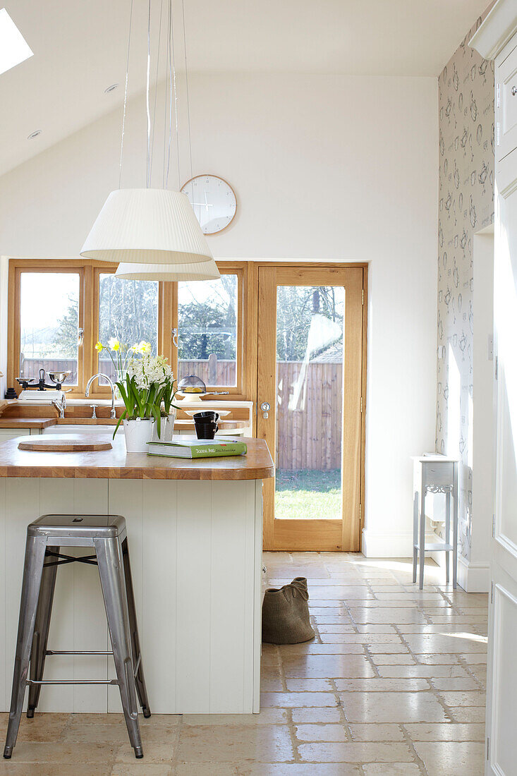 Open plant kitchen with cream pendant lights and wood framed doors in Kent home, England, UK
