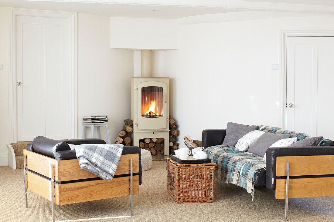 Tea tray on basket with wooden three-piece suite in living room with lit woodburning stove in Kent home, England, UK