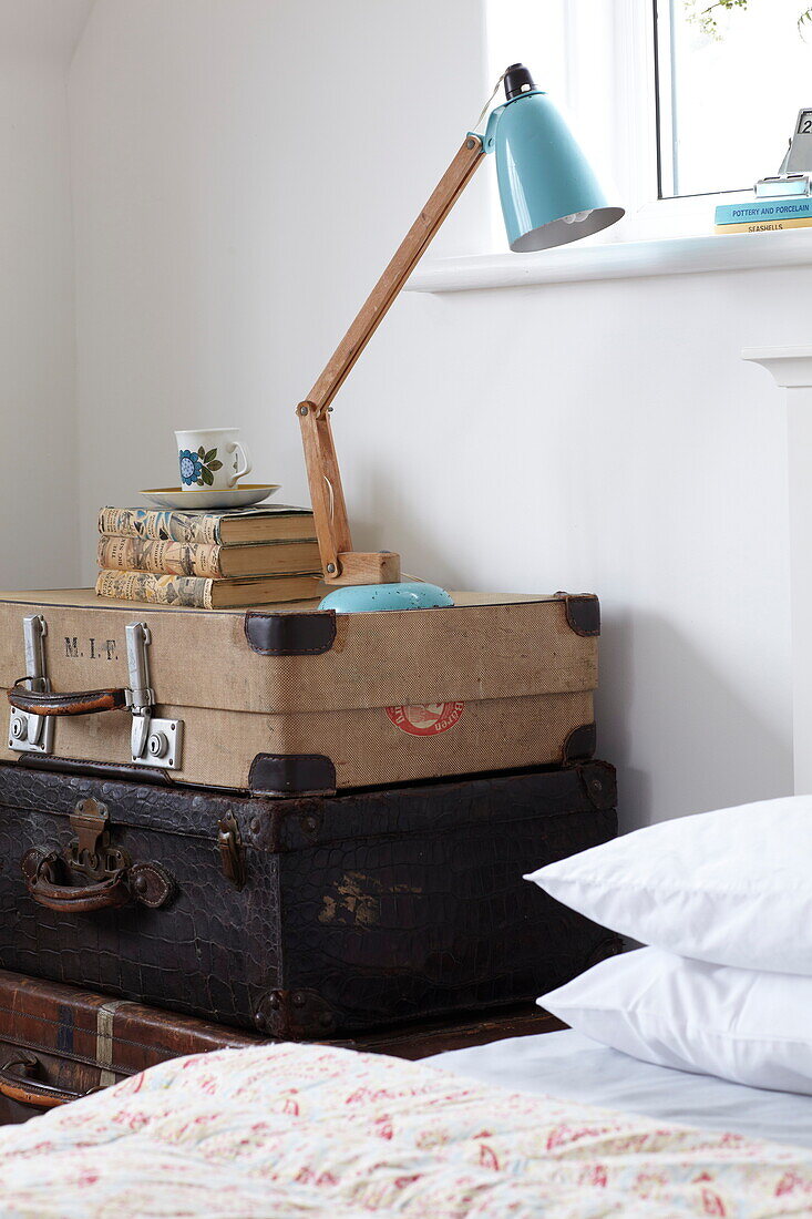 Anglepoise lamp on stack of vintage suitcases at bedside in Bembridge home, Isle of Wight, UK