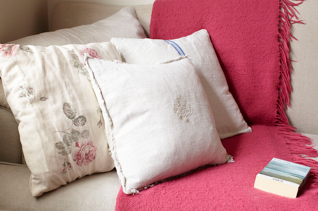Leinenkissen mit rosa Decke und Buch auf Sofa in Doppelhaushälfte, UK