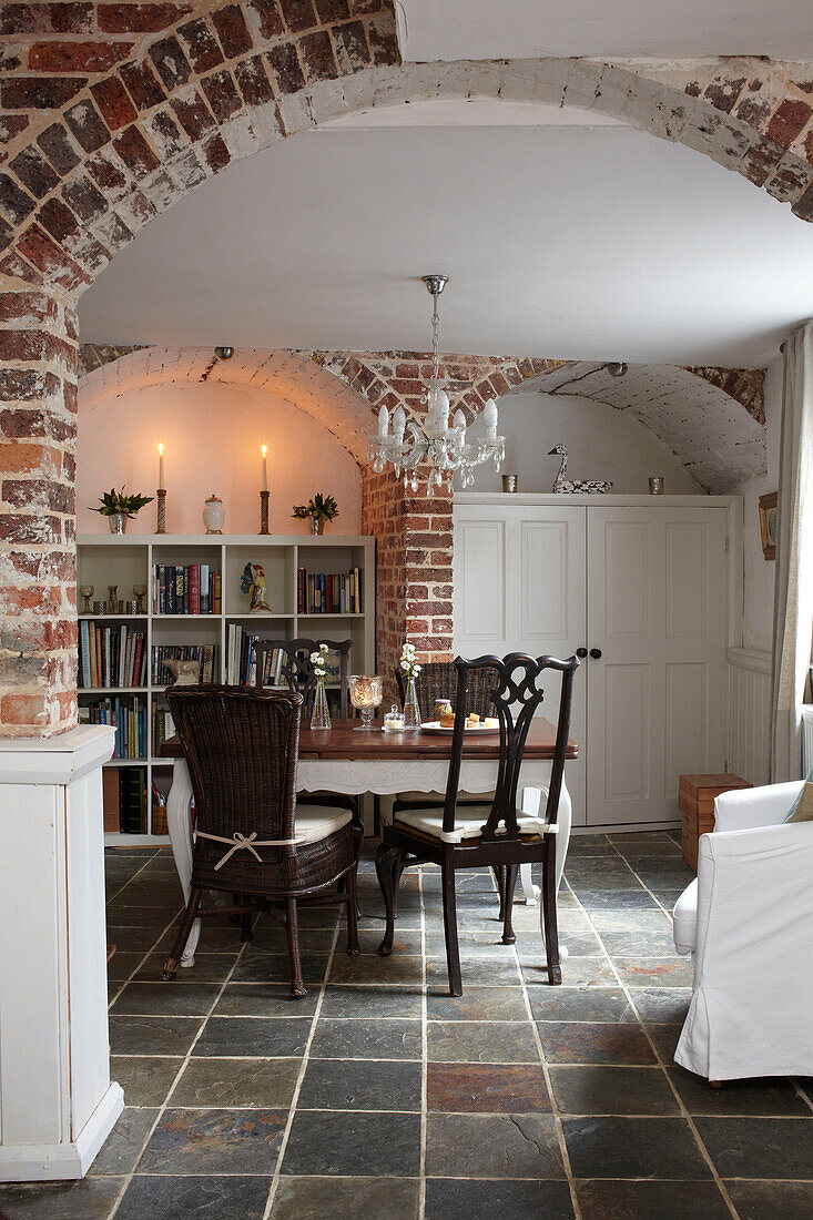 Dining table and chairs with bookcase and exposed brick archway in open plan interior of semi-detached home UK