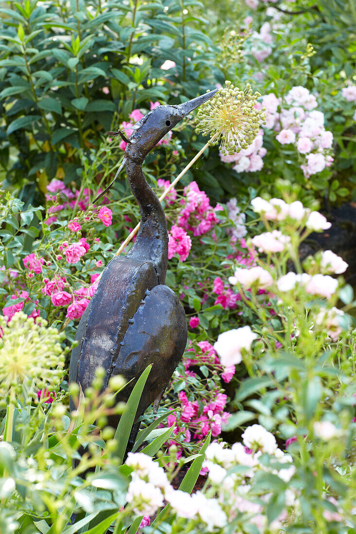 Heron sculpture with pink roses in Wiltshire garden, England, UK