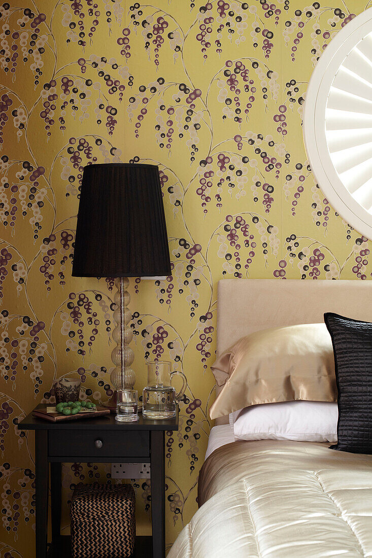Patterned wallpaper and black bedside lamp in bedroom of London home England UK