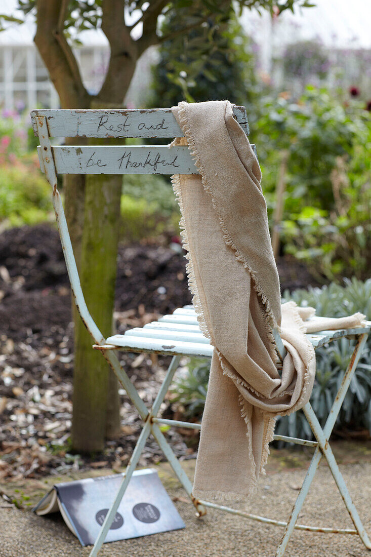 Folding chair with handwriting 'Rest and be thankful' in garden, St Lawrence, Isle of Wight, UK