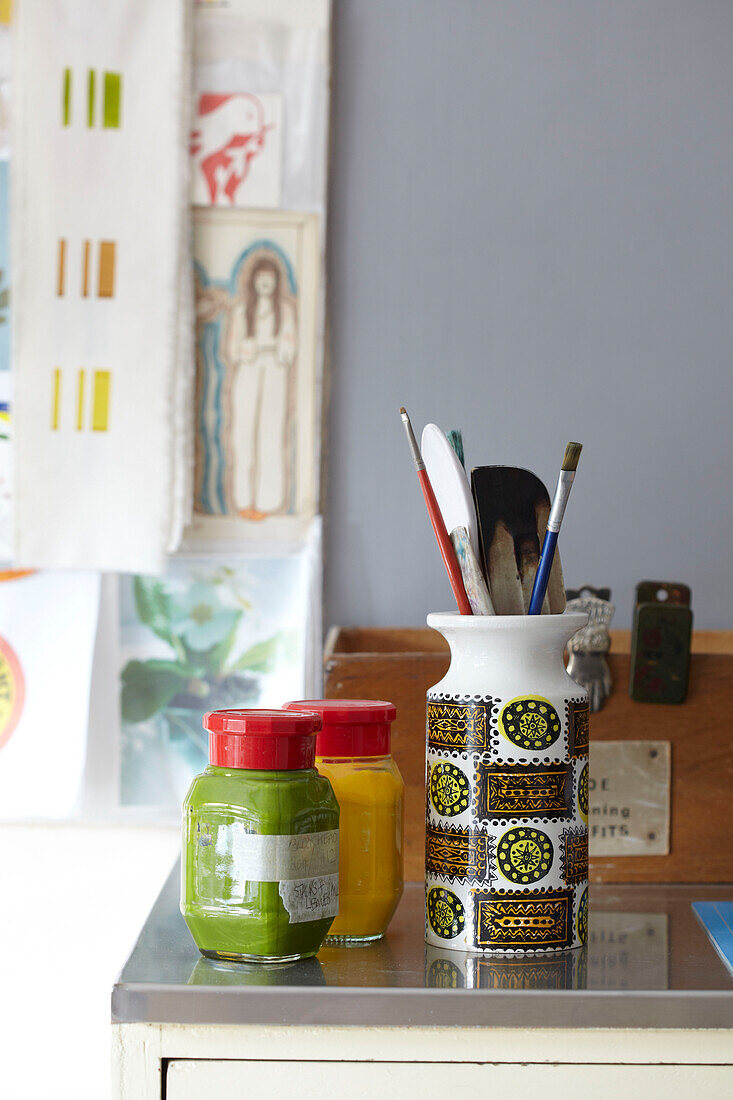 Green and yellow paint with brushes in retro styled jar in Ryde work studio Isle of Wight, UK