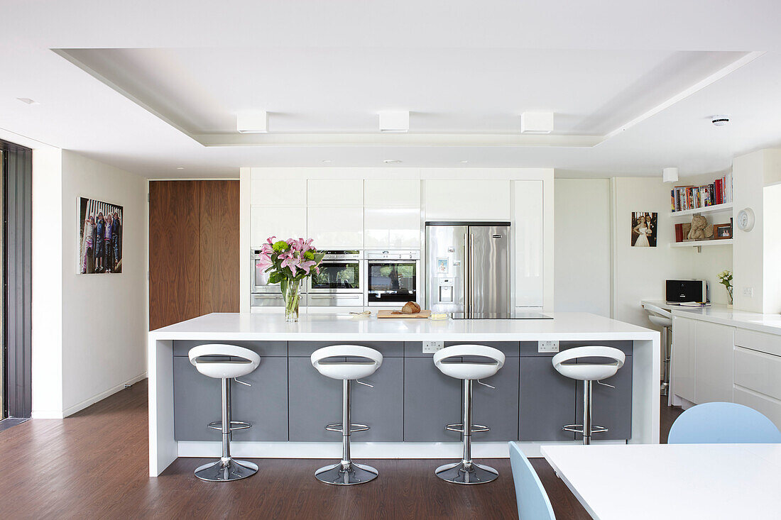 Four bar stools with cut lilies on breakfast bar in modern interior of Isle of Wight home UK
